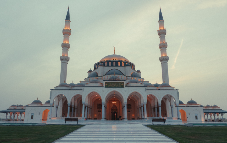 Sharjah Mosque with its domes and two tall minarets lit up at dusk