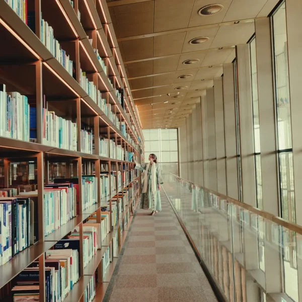 Helena browsing the long wall of bookshelves beside floor-to-ceiling windows at the House of Wisdom, Sharjah
