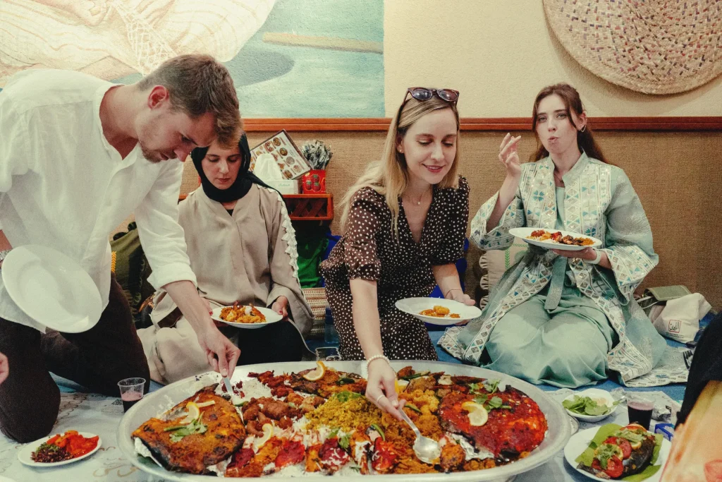 Friends sharing a giant grilled and fried fish platter while sitting on the floor at Al Banosh, Sharjah
